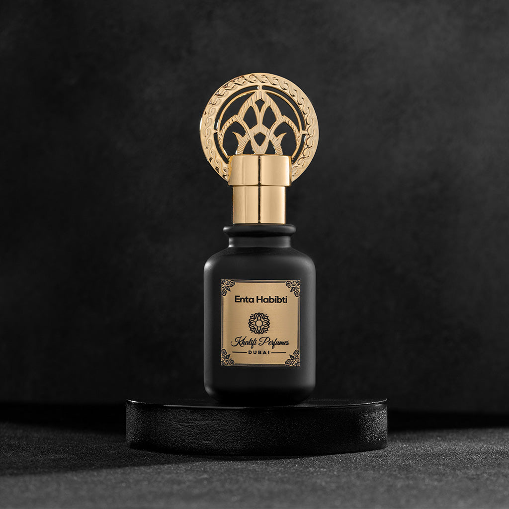 Black bottle gold cap oriental perfume Enta Habibti by Khalifi Perfumes on a black wooden rounded piece of wood and a black background