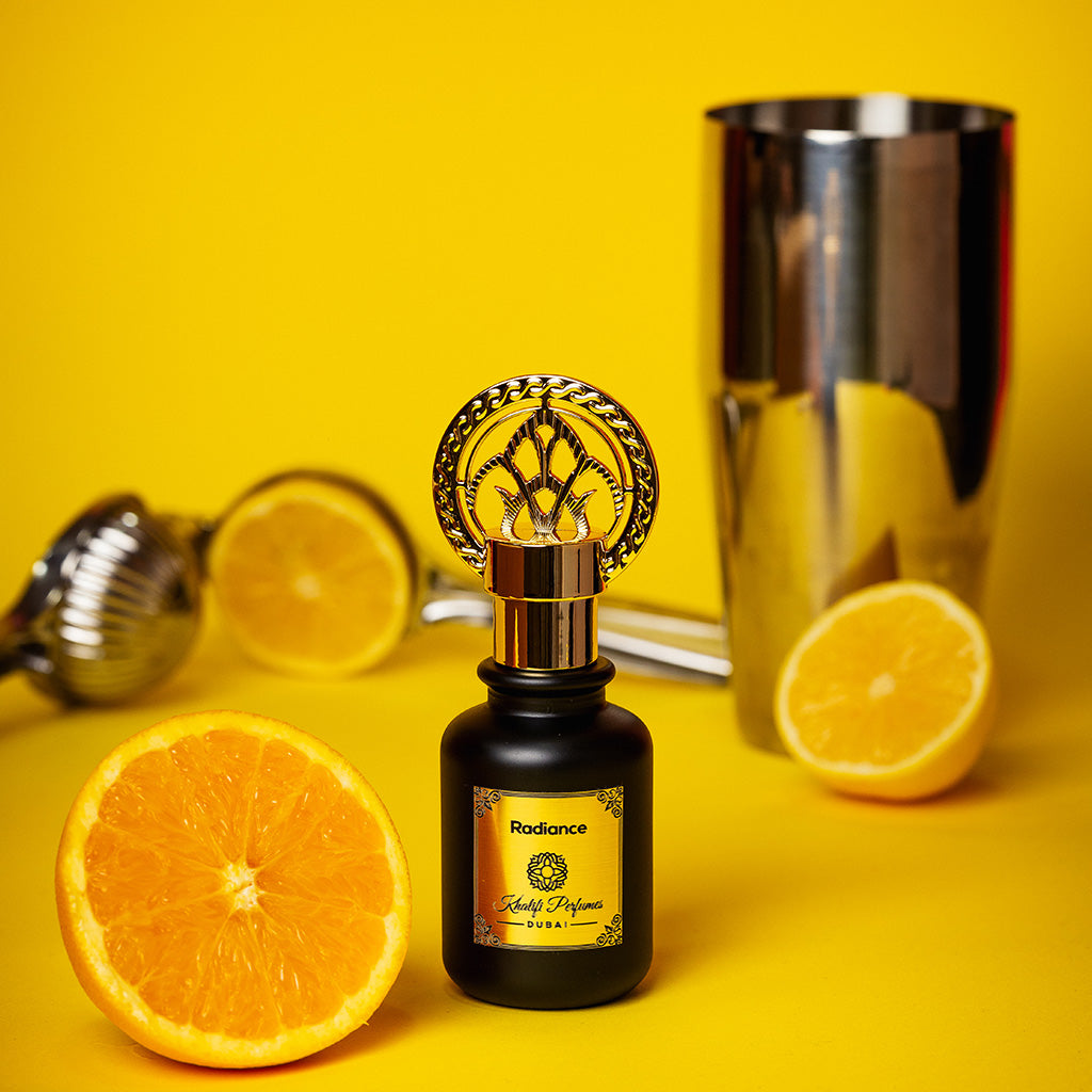 Black bottle with golden cap perfume Radience by Khalifi Perfumes with oranges next to it and a shaker behind, on a orange background